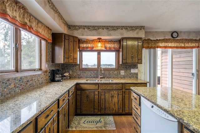 kitchen with backsplash, dishwasher, sink, and light hardwood / wood-style floors