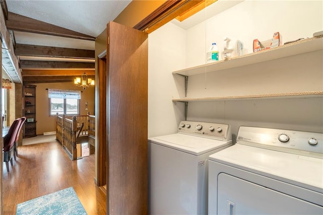 clothes washing area featuring washer and clothes dryer, a notable chandelier, and light hardwood / wood-style flooring