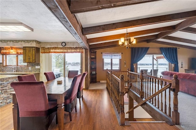 dining area with sink, an inviting chandelier, lofted ceiling with beams, light hardwood / wood-style floors, and a textured ceiling