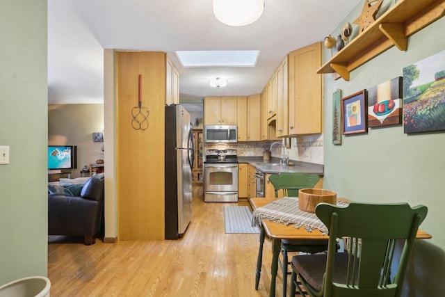 kitchen with light brown cabinetry, tasteful backsplash, stainless steel appliances, sink, and light hardwood / wood-style floors