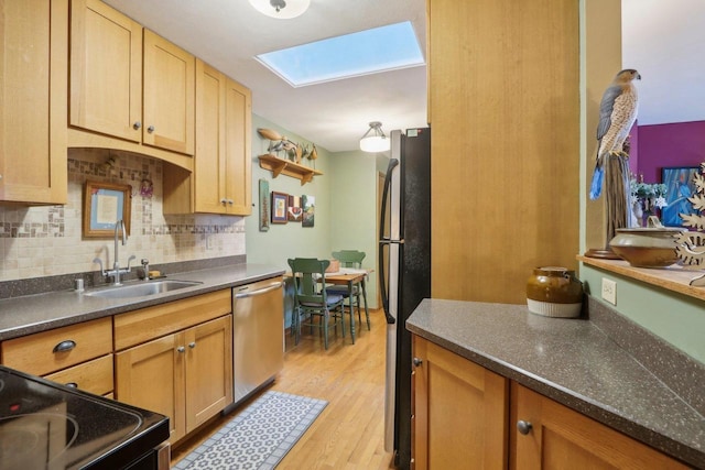 kitchen with dishwasher, black refrigerator, sink, a skylight, and light hardwood / wood-style floors