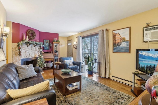 living room with a stone fireplace, wood-type flooring, baseboard heating, and a wall mounted AC