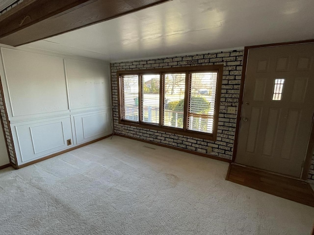 carpeted foyer entrance featuring beamed ceiling and brick wall