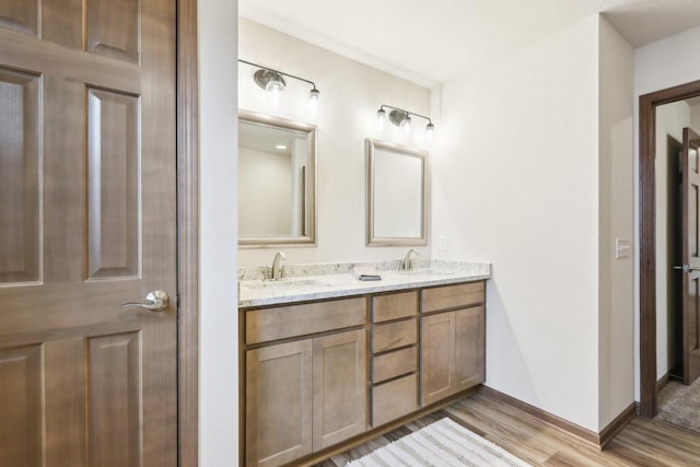 full bath with double vanity, baseboards, a sink, and wood finished floors