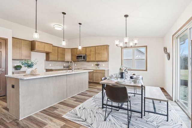 kitchen featuring light wood-style floors, vaulted ceiling, hanging light fixtures, tasteful backsplash, and a center island with sink