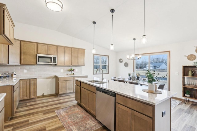 kitchen featuring light wood finished floors, tasteful backsplash, appliances with stainless steel finishes, a sink, and light stone countertops