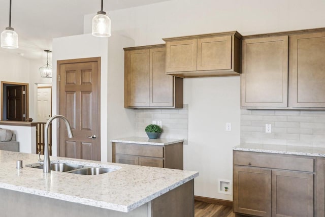 kitchen with light stone counters, decorative light fixtures, tasteful backsplash, dark wood-type flooring, and a sink