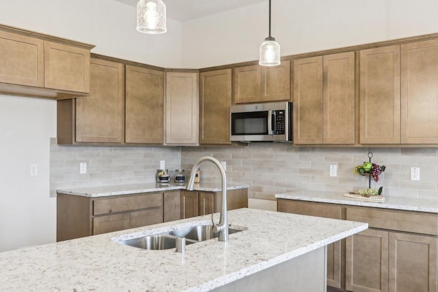 kitchen with stainless steel microwave, hanging light fixtures, decorative backsplash, a sink, and light stone countertops