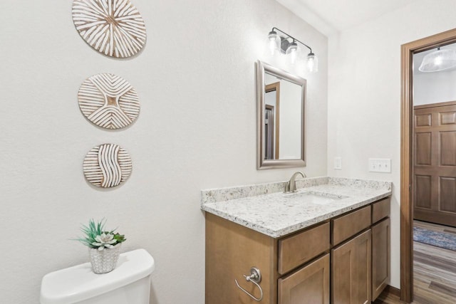 half bathroom featuring toilet, wood finished floors, and vanity