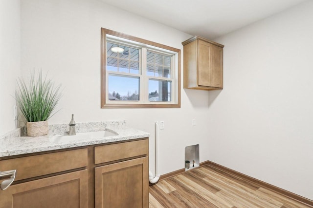 clothes washing area featuring baseboards, cabinet space, a sink, and light wood finished floors