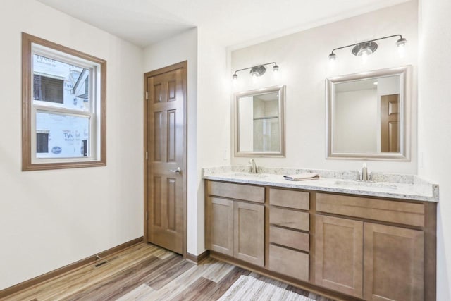 full bathroom with double vanity, wood finished floors, a sink, and baseboards