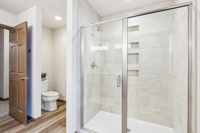 bathroom with baseboards, wood finished floors, toilet, and a shower stall