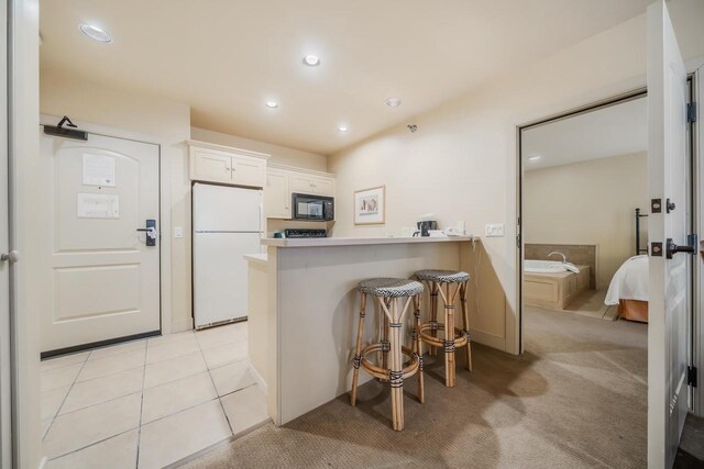 kitchen with white cabinetry, a kitchen breakfast bar, kitchen peninsula, white fridge, and light carpet