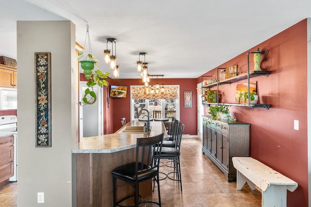 kitchen featuring a kitchen breakfast bar, white appliances, sink, pendant lighting, and a notable chandelier