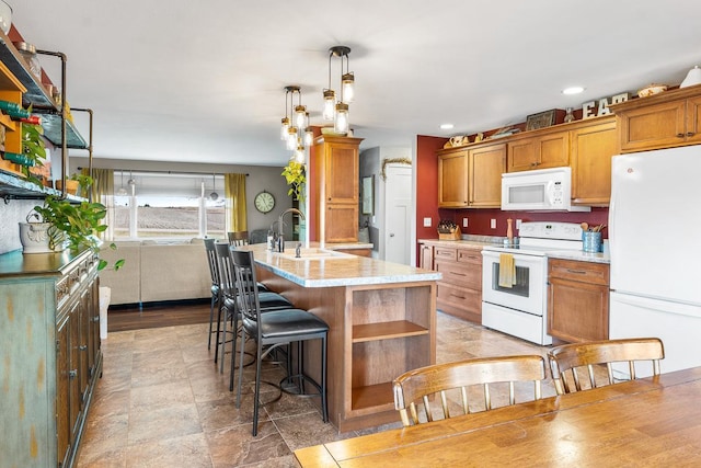 kitchen with sink, hanging light fixtures, light stone counters, white appliances, and a center island with sink