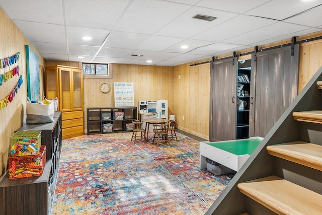 game room featuring a barn door, wooden walls, and a paneled ceiling