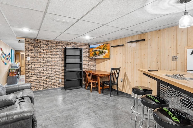 bar with decorative light fixtures, a drop ceiling, wood walls, and brick wall