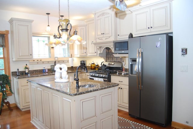 kitchen with sink, stainless steel appliances, an island with sink, dark stone counters, and pendant lighting