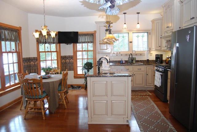 kitchen featuring a center island with sink, hanging light fixtures, black range with gas cooktop, and stainless steel refrigerator