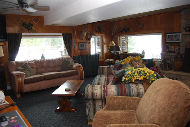 living room with dark colored carpet, ceiling fan, wood walls, and baseboard heating