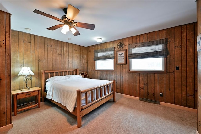 carpeted bedroom featuring multiple windows, ceiling fan, and wooden walls