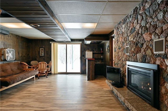 interior space featuring a fireplace, light wood-type flooring, a paneled ceiling, and wood walls