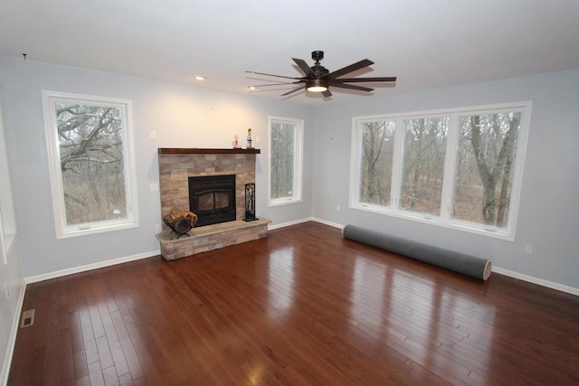 unfurnished living room featuring a stone fireplace, a wealth of natural light, ceiling fan, and dark hardwood / wood-style floors