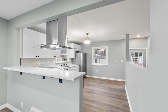 kitchen with a kitchen breakfast bar, island exhaust hood, kitchen peninsula, decorative light fixtures, and white cabinets