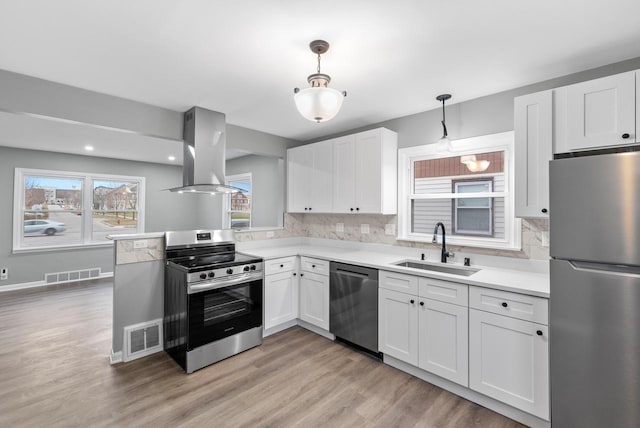 kitchen with stainless steel appliances, island range hood, sink, decorative light fixtures, and white cabinets