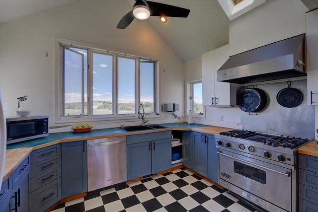 kitchen with appliances with stainless steel finishes, wall chimney exhaust hood, vaulted ceiling with skylight, sink, and butcher block countertops