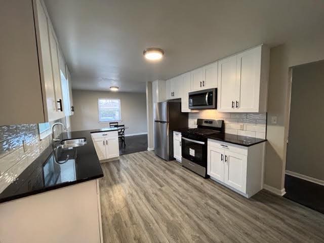 kitchen with white cabinets, sink, decorative backsplash, light wood-type flooring, and stainless steel appliances