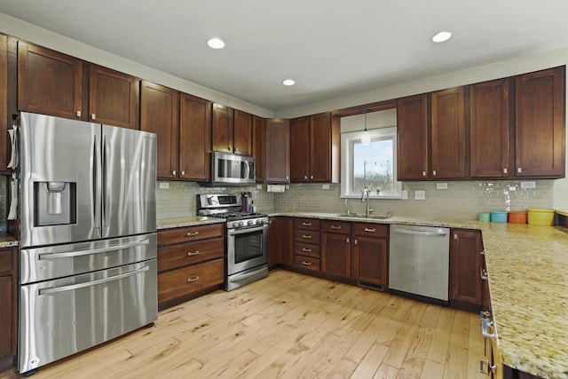 kitchen featuring light stone countertops, light wood-type flooring, backsplash, stainless steel appliances, and sink