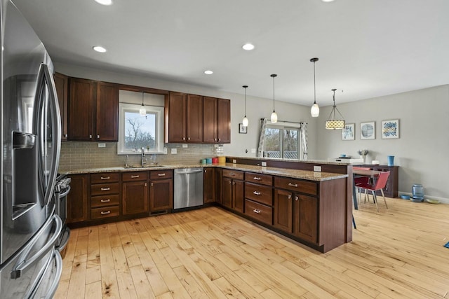 kitchen with kitchen peninsula, appliances with stainless steel finishes, decorative light fixtures, and a wealth of natural light