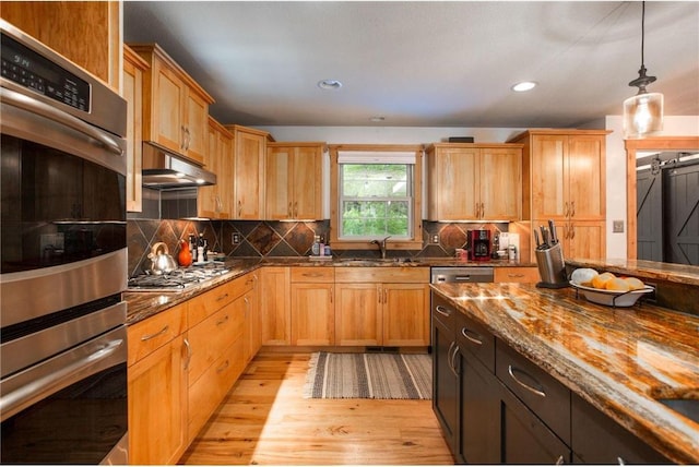 kitchen with stainless steel appliances, sink, pendant lighting, light hardwood / wood-style flooring, and dark stone countertops