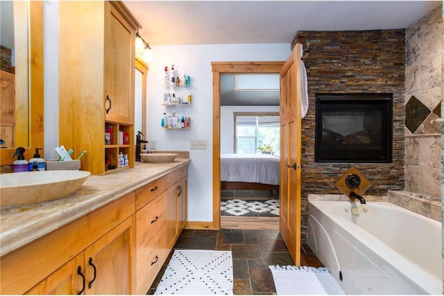 bathroom with vanity, a bathtub, a stone fireplace, and a textured ceiling