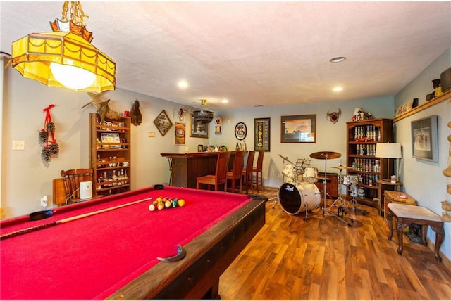 recreation room featuring wood-type flooring, a textured ceiling, bar, and pool table