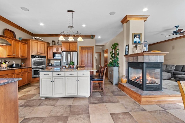 kitchen featuring a kitchen breakfast bar, stainless steel appliances, decorative light fixtures, an island with sink, and a tiled fireplace