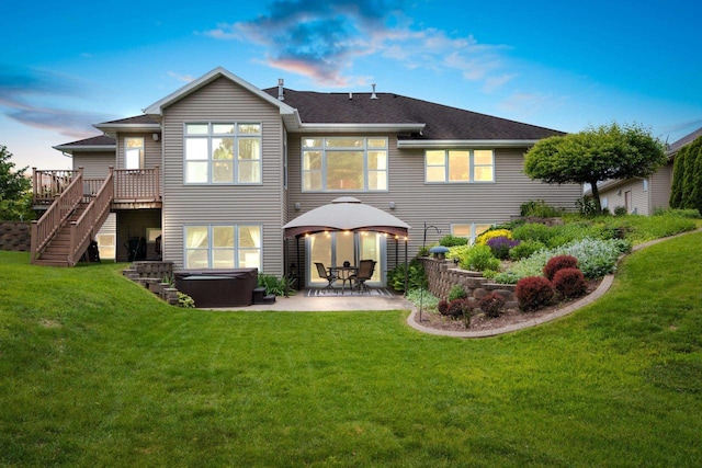 back house at dusk featuring a lawn, a deck, a hot tub, a gazebo, and a patio area