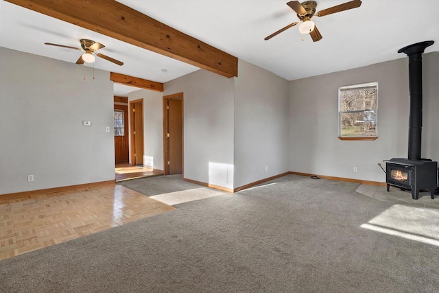 unfurnished living room with beamed ceiling, ceiling fan, a wood stove, and light parquet flooring