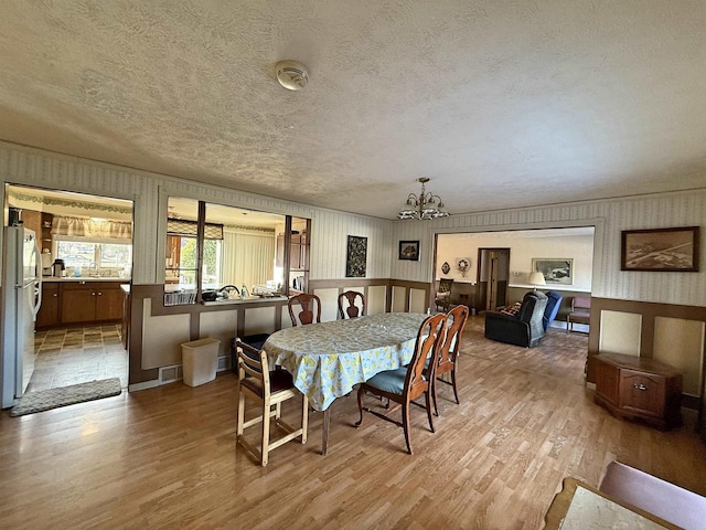 dining space with an inviting chandelier, a textured ceiling, and light wood-type flooring