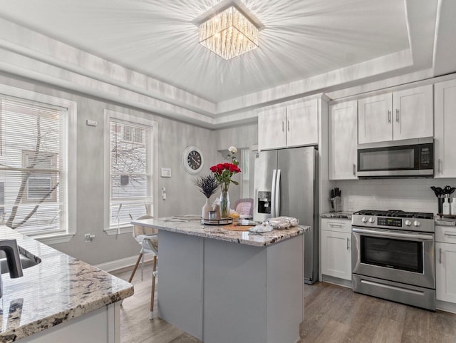 kitchen with light stone counters, white cabinets, light wood-type flooring, and appliances with stainless steel finishes