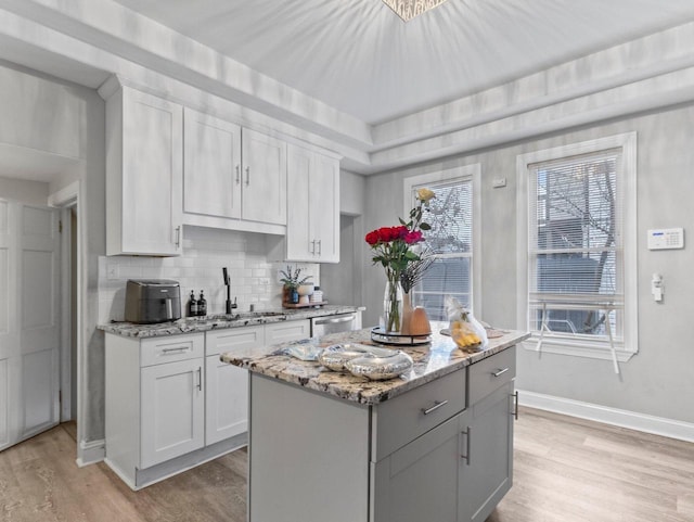 kitchen featuring sink, light stone countertops, light wood-type flooring, tasteful backsplash, and a kitchen island