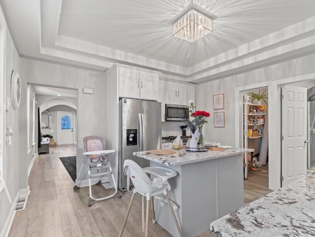 kitchen featuring a breakfast bar, light stone countertops, appliances with stainless steel finishes, a tray ceiling, and white cabinetry