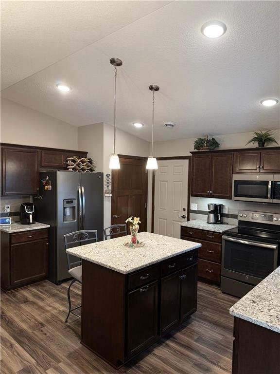 kitchen featuring dark hardwood / wood-style floors, a kitchen island, stainless steel appliances, and vaulted ceiling