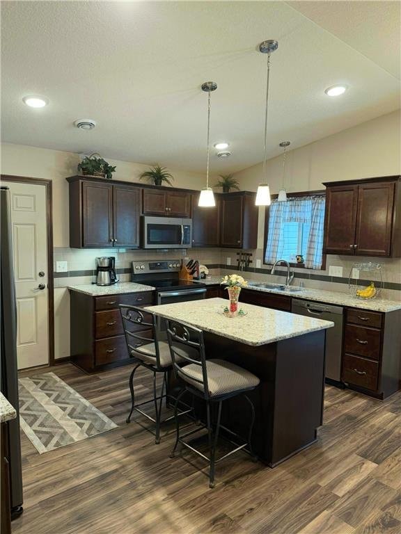 kitchen with appliances with stainless steel finishes, vaulted ceiling, dark hardwood / wood-style floors, a kitchen island, and hanging light fixtures