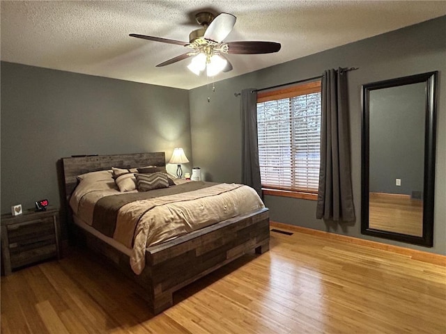 bedroom with a textured ceiling, light wood-type flooring, and ceiling fan