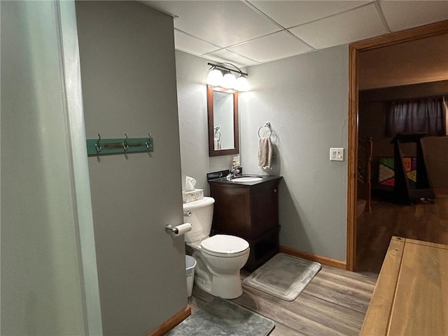 bathroom with a paneled ceiling, vanity, wood-type flooring, and toilet