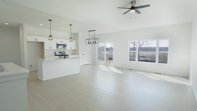 unfurnished living room with a wealth of natural light, light wood-style flooring, a ceiling fan, and a sink