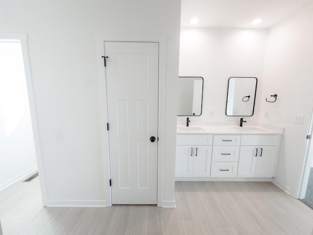 full bathroom featuring a sink, baseboards, wood finished floors, and double vanity