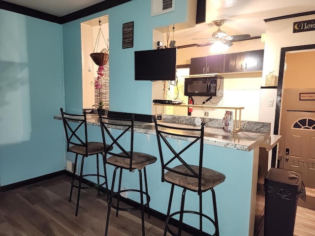 kitchen featuring a kitchen bar, kitchen peninsula, ceiling fan, and dark hardwood / wood-style floors